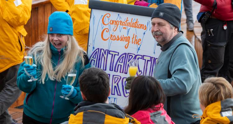 Cérémonie à bord avec des passagers portant un toast à côté d'une pancarte dessinée à la main célébrant le franchissement du Cercle Antarctique.