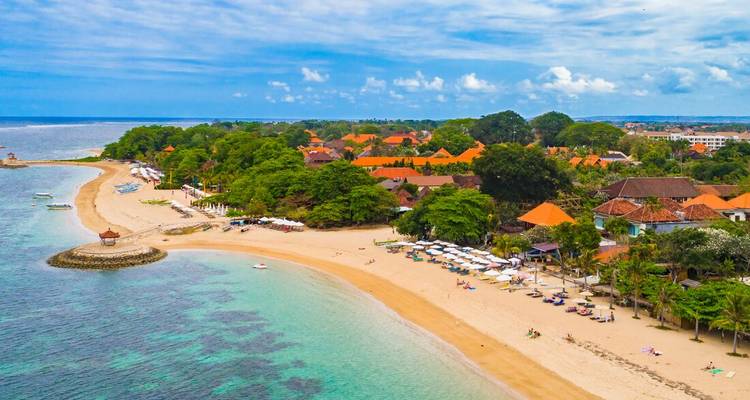 Vue aérienne d'une plage de sable avec une végétation luxuriante et un complexe hôtelier.