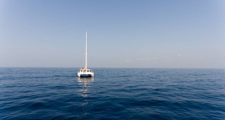 Un catamarán solitario flota en el océano azul abierto bajo un cielo despejado