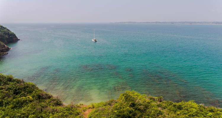 Vista aérea con dron de aguas turquesas y un catamarán anclado cerca de una costa exuberante