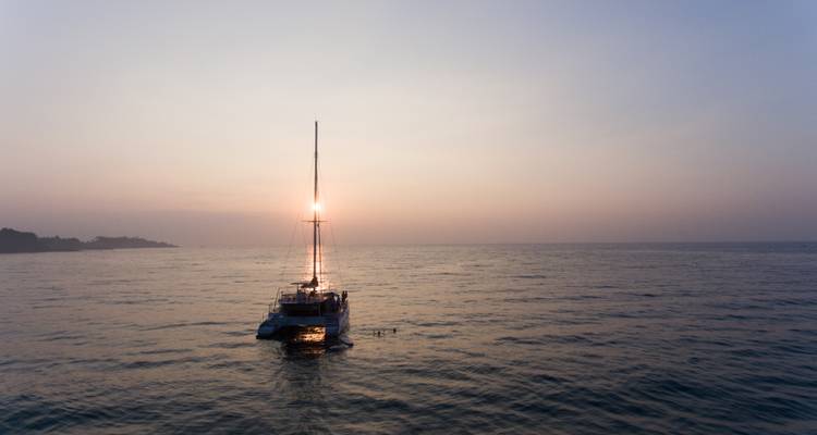 Un catamarán recortado contra una puesta de sol pastel con mares tranquilos