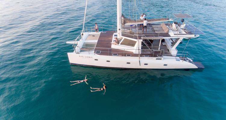 Los viajeros se relajan y nadan junto a un elegante catamarán blanco en aguas cristalinas