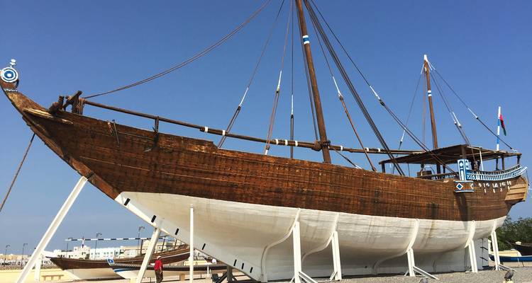 Un gran dhow tradicional de madera exhibido sobre soportes bajo un cielo despejado.