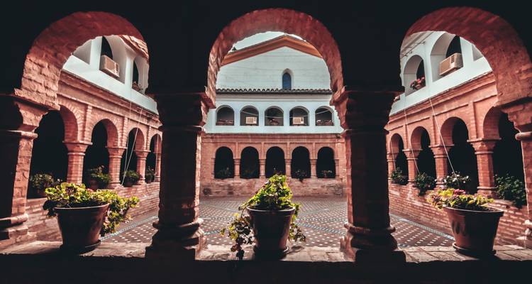 Un patio pintoresco con plantas en macetas, enmarcado por arcos.