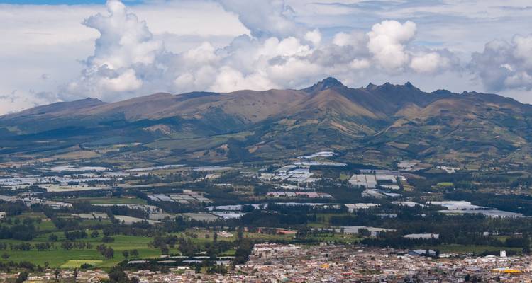 Vista panorámica amplia de valles fértiles y campos de retazos con picos andinos bajo nubes cúmulos