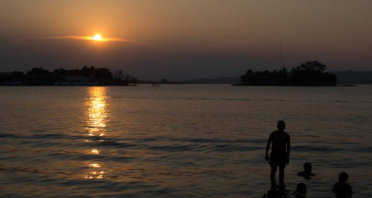 Personas silueteadas vadiendo en un lago tranquilo durante una puesta de sol dorada