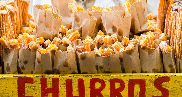 Des piles de churros saupoudrés de sucre dans des sacs en papier brun tentent à un stand de nourriture de rue.