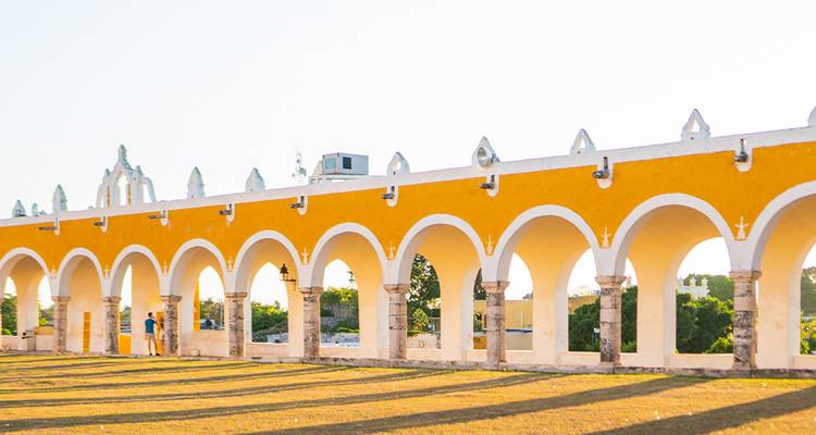 La longue arcade jaune du Couvent d'Izamal brille dans la lumière de fin d'après-midi tandis que les visiteurs se promènent en dessous.