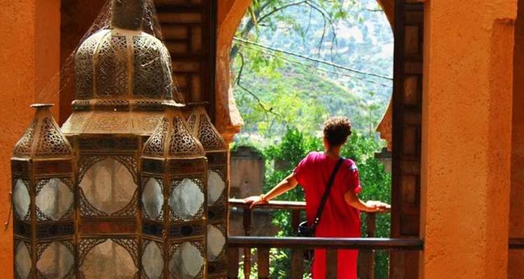 Personne en tenue traditionnelle regardant un paysage à travers une fenêtre en pierre.