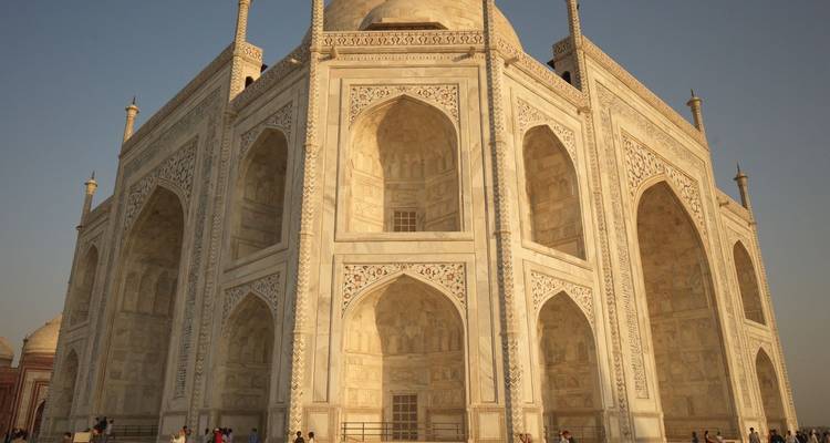 Vue en contre-plongée du Taj Mahal en marbre blanc ivoire brillant sous une lumière chaude avec de petits visiteurs à sa base.