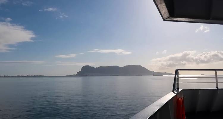 Kalm zeezicht vanaf een veerboot met silhouet van Gibraltar-achtige rots aan de horizon