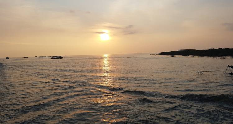 Una puesta de sol serena sobre un vasto lago con pequeños botes en el horizonte.