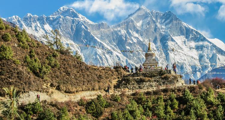 Mit Gebetsfahnen gesäumter Wanderweg mit Trekkern und einer Stupa mit Blick auf Mounts Everests eisigen Gipfel.