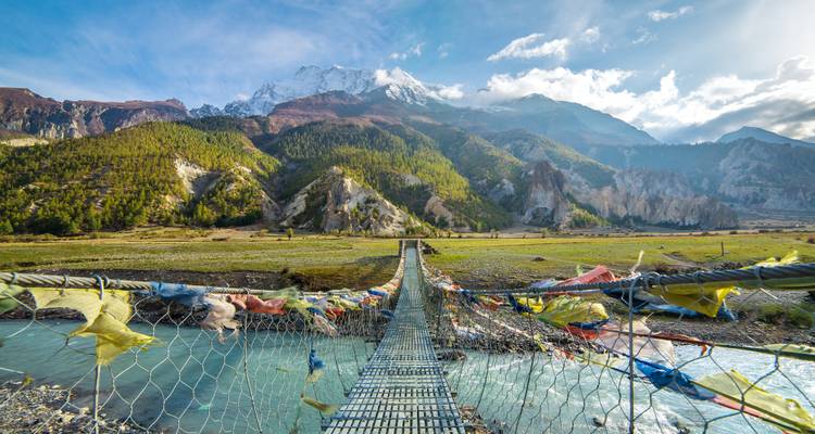 Hangbrug behangen met gebedsvaandels over een gletsjerivier onder het Annapurna-massief.