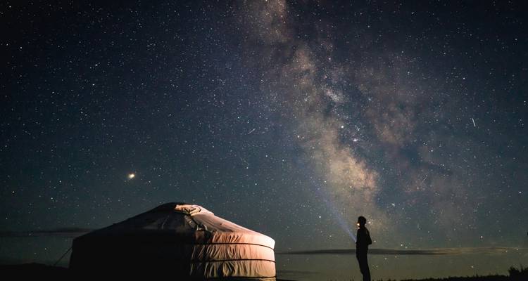 Una figura solitaria junto a una yurta contempla un deslumbrante cielo de Vía Láctea mientras un rayo de luz señala las estrellas.