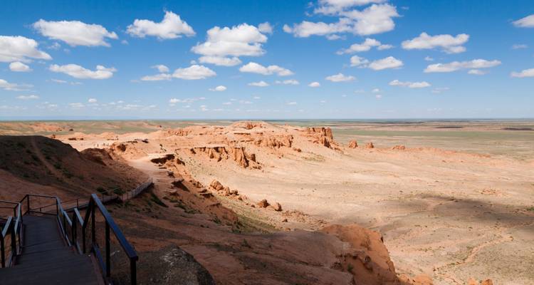 Los acantilados de arenisca roja de Bayanzag se extienden a lo largo de una llanura desértica plana bajo un cielo salpicado de nubes blancas.