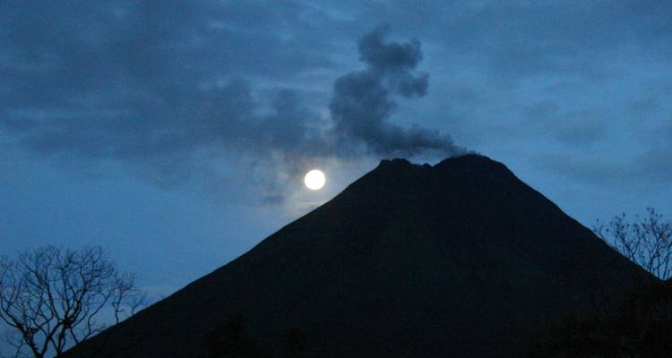 Silhouette de volcan avec fumée sur fond de ciel lunaire.