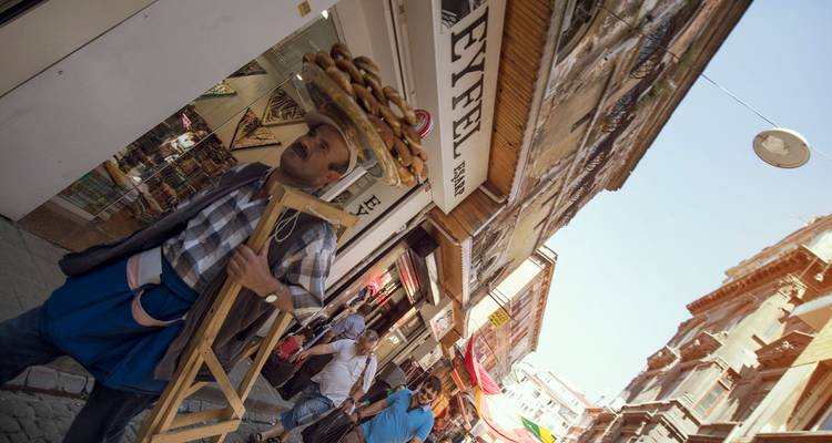 Vendeur ambulant équilibrant un plateau de simit tandis que des clients affairés passent dans une ruelle animée d'Istanbul.