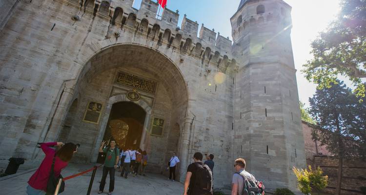 Les visiteurs franchissent la porte en pierre ornementée du Palais de Topkapi d'Istanbul sous un soleil éclatant.