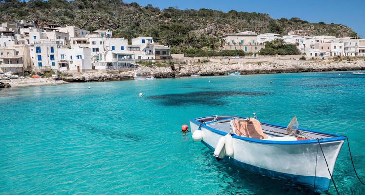 Bahía de un azul turquesa cristalino con una solitaria embarcación anclada cerca de casitas blancas frente al mar y una costa rocosa.