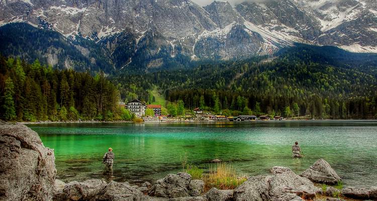 Lago verde con fondo montañoso, pocas personas pescando en el agua.