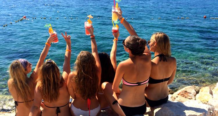 Grupo de mujeres levantando bebidas de colores junto al mar.