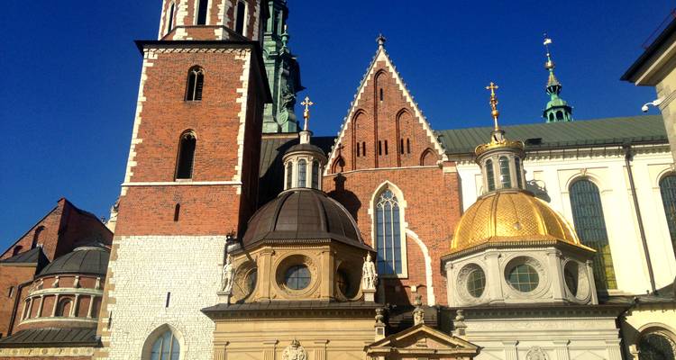 Vue rapprochée de la tour en brique de la Cathédrale de Wawel et de ses chapelles aux dômes dorés sur un ciel bleu profond
