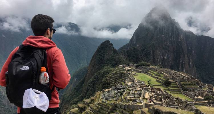Personne surplombant les ruines du Machu Picchu et les montagnes couvertes de nuages.