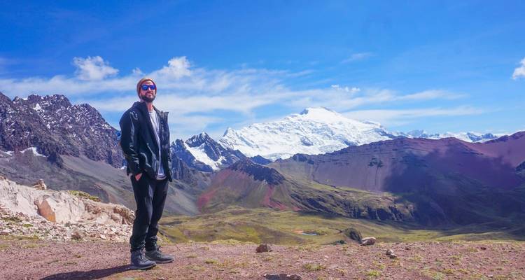 Homme posant avec un vaste paysage de montagnes et un ciel bleu.