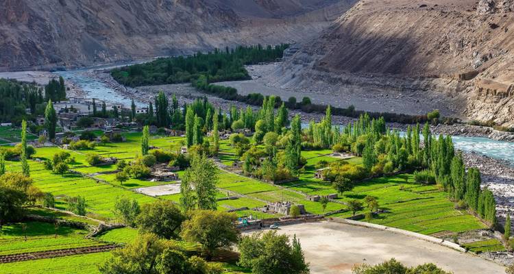 Verdant valley with patchwork of green fields and a turquoise river winding below steep brown mountains.