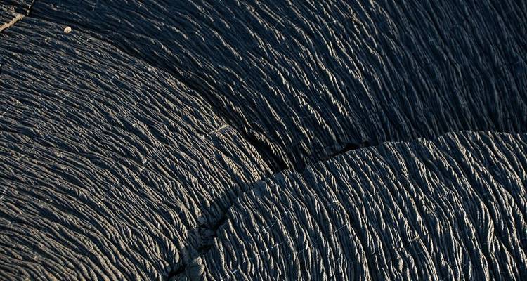 Texture abstraite en gros plan de lave durcie présentant des ondulations et des motifs complexes.