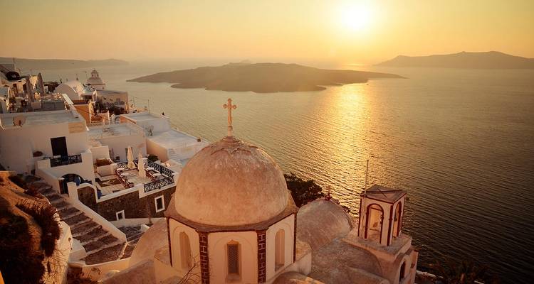 Iglesia icónica con cúpula que domina la caldera al atardecer en Santorini con luz dorada reflejándose en el mar.