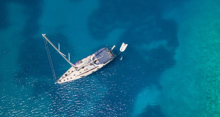 Luftaufnahme einer eleganten Segelyacht, die in den glänzenden türkisfarbenen Gewässern einer griechischen Insel schwebt.