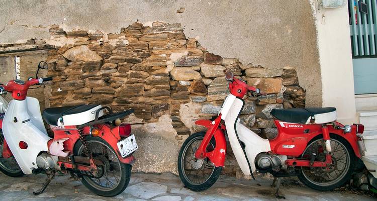 Dos scooters vintage rojos y blancos estacionados al lado de una pared de piedra y yeso rústica.