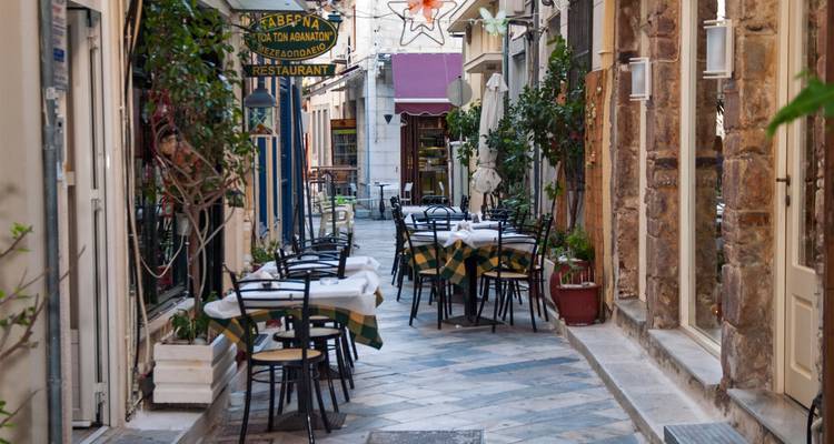 Un encantador callejón estrecho lleno de mesas y sillas afuera de una taberna tradicional en Grecia.