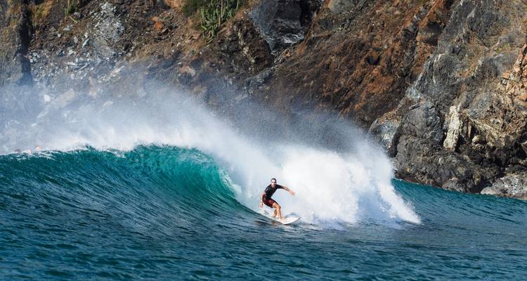 Surfeur chevauchant une grosse vague près d'un rivage rocheux.