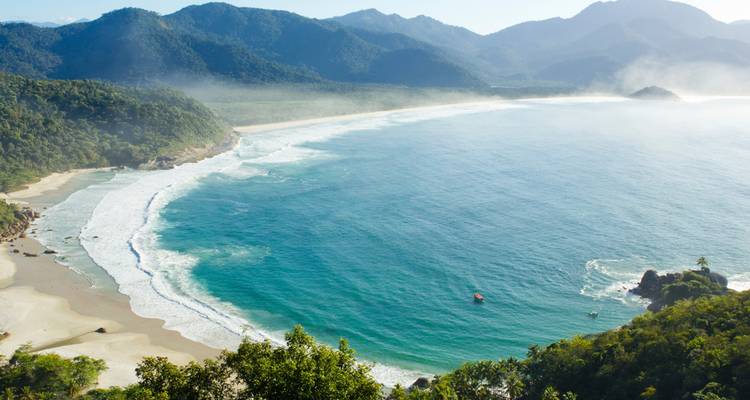 Vista aérea panorámica de una bahía extensa con agua esmeralda y montañas boscosas brumosas en Ilha Grande.