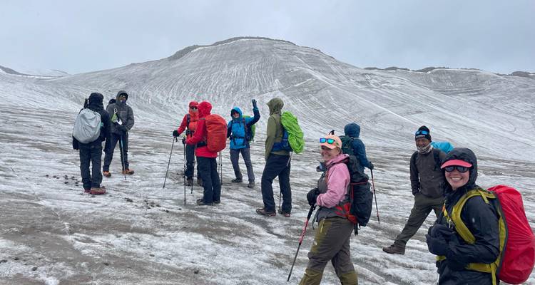 Des randonneurs vêtus de vestes colorées traversent une crête enneigée dans des conditions venteuses en montagne.