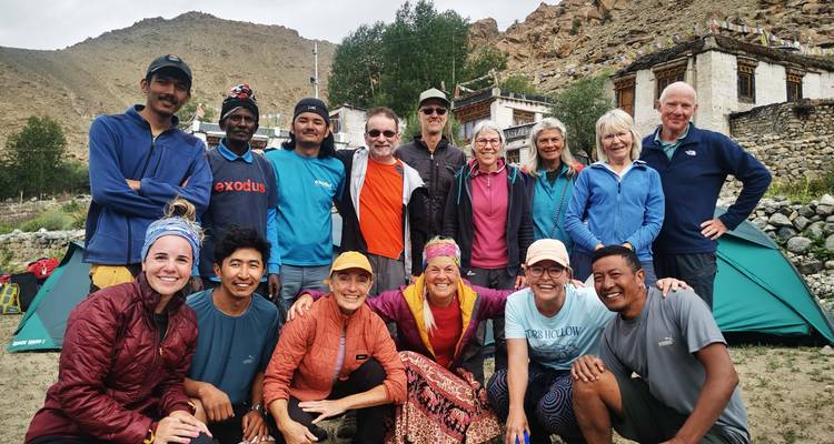 Les trekkeurs et l'équipe locale se rassemblent pour une photo de groupe joyeuse au campement de l'Himalaya avec des tentes vertes derrière eux.