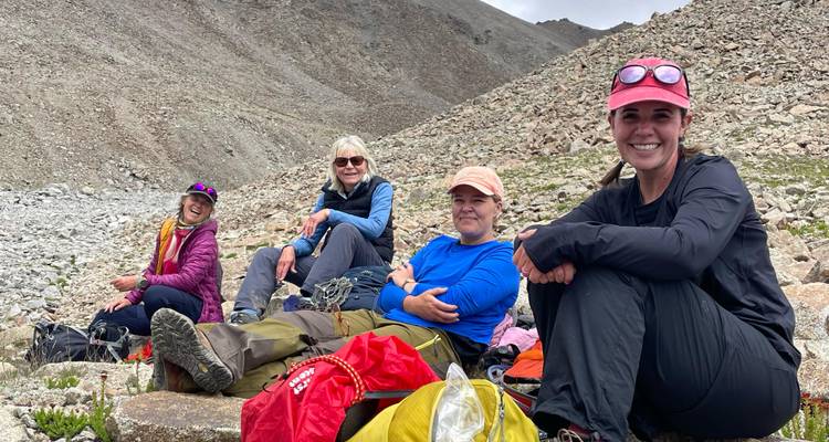 Quatre randonneurs sont assis sur un terrain rocailleux et font une pause, souriants au milieu d'un paysage désertique d'haute altitude.