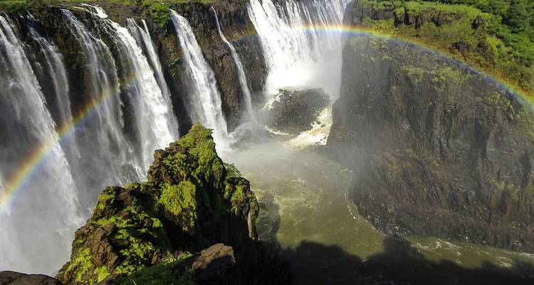De imposante Victoria Falls storting zich in een mistige kloof met een levendige regenboog die erover heen bogen.