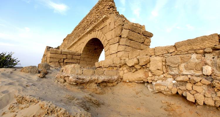 Arche de pierre en ruines dans un décor désertique.