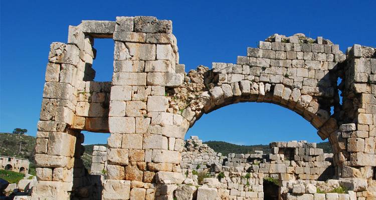 Arco de piedra desgastada y bloques de una ruina antigua contra un cielo azul brillante en la región de Antalya.