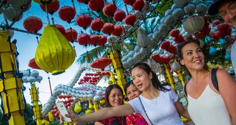 Viajeros felices tomándose selfies bajo los doseletes de linternas brillantes en Hoi An.