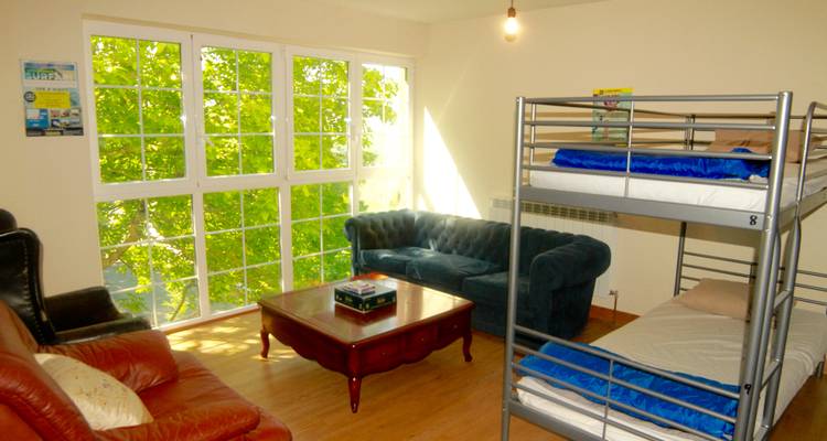 Innenraum eines Zimmers mit Etagenbetten und Sofas, draußen Sonne.