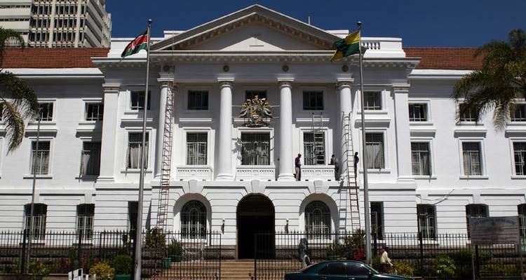 White colonial-style government building with flags and a car in front.