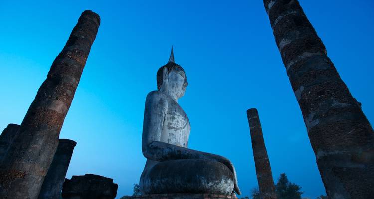 Statue de Bouddha parmi les piliers anciens au crépuscule.