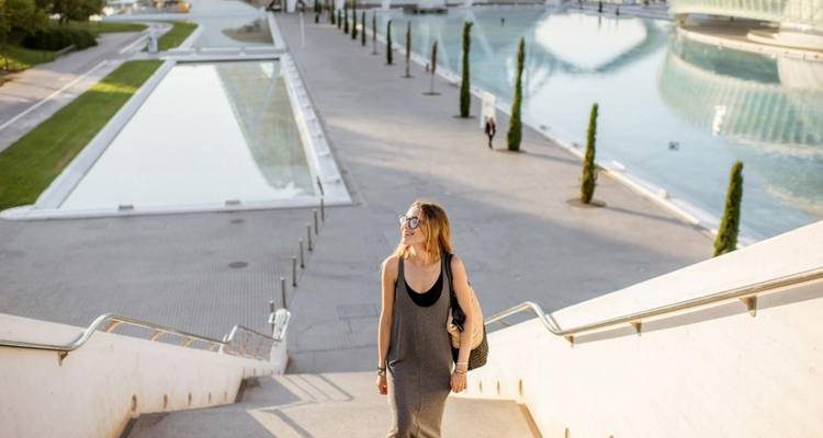 Eine Frau, die eine Treppe hinaufgeht, mit moderner Architektur und Pools im Hintergrund.
