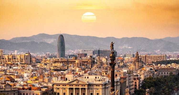Eine Stadtskyline mit einer markanten Säule und der Sonne, die über den Bergen untergeht.