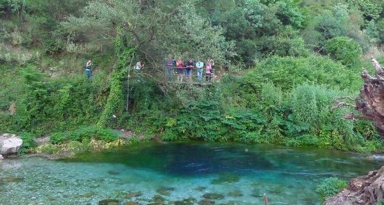 Toeristen bij een heldere blauwe bron omringd door weelderig groen.